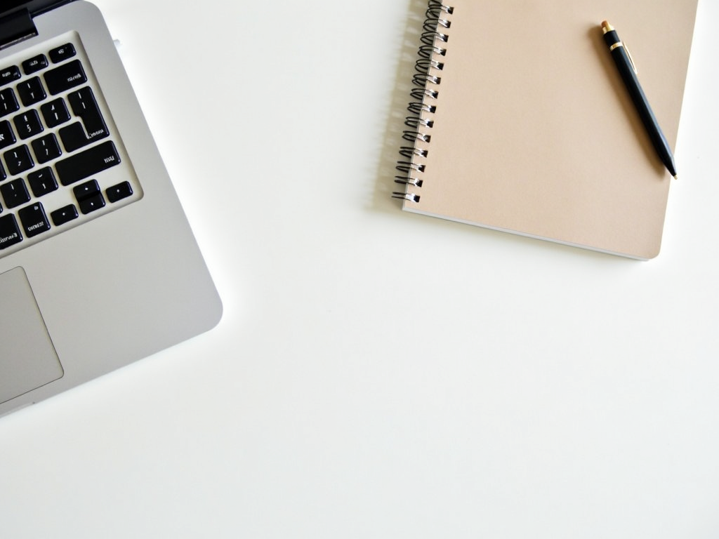 Minimalistischer Arbeitsplatz mit Laptop, Notizbuch und Stift.